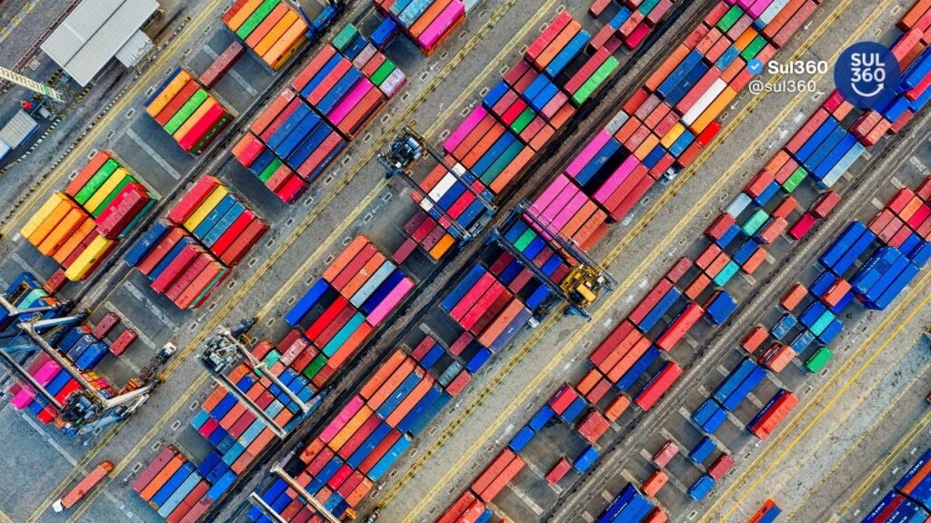 Contêineres coloridos empilhados em terminal portuário visto de cima com guindastes operando exportações do RS